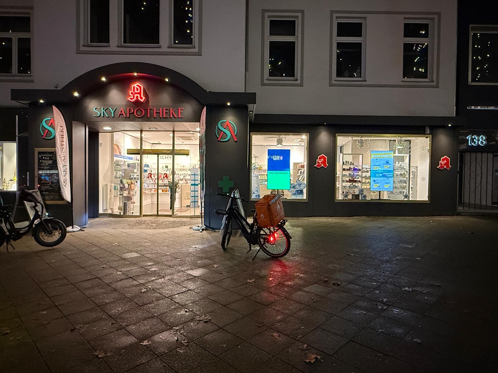 Sky Apotheke Kudamm mit zwei beleuchteten digitalen Schaufensterdisplays am Abend